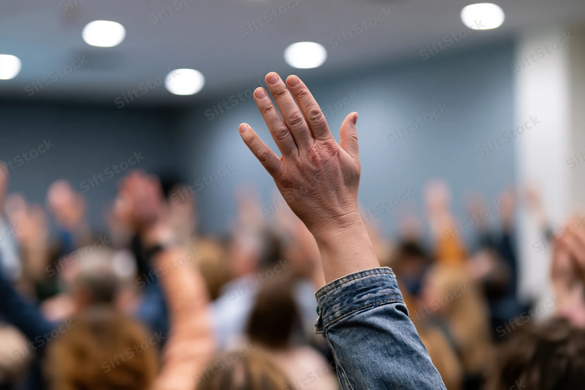 Raised hand in foreground during group meeting with audience in background