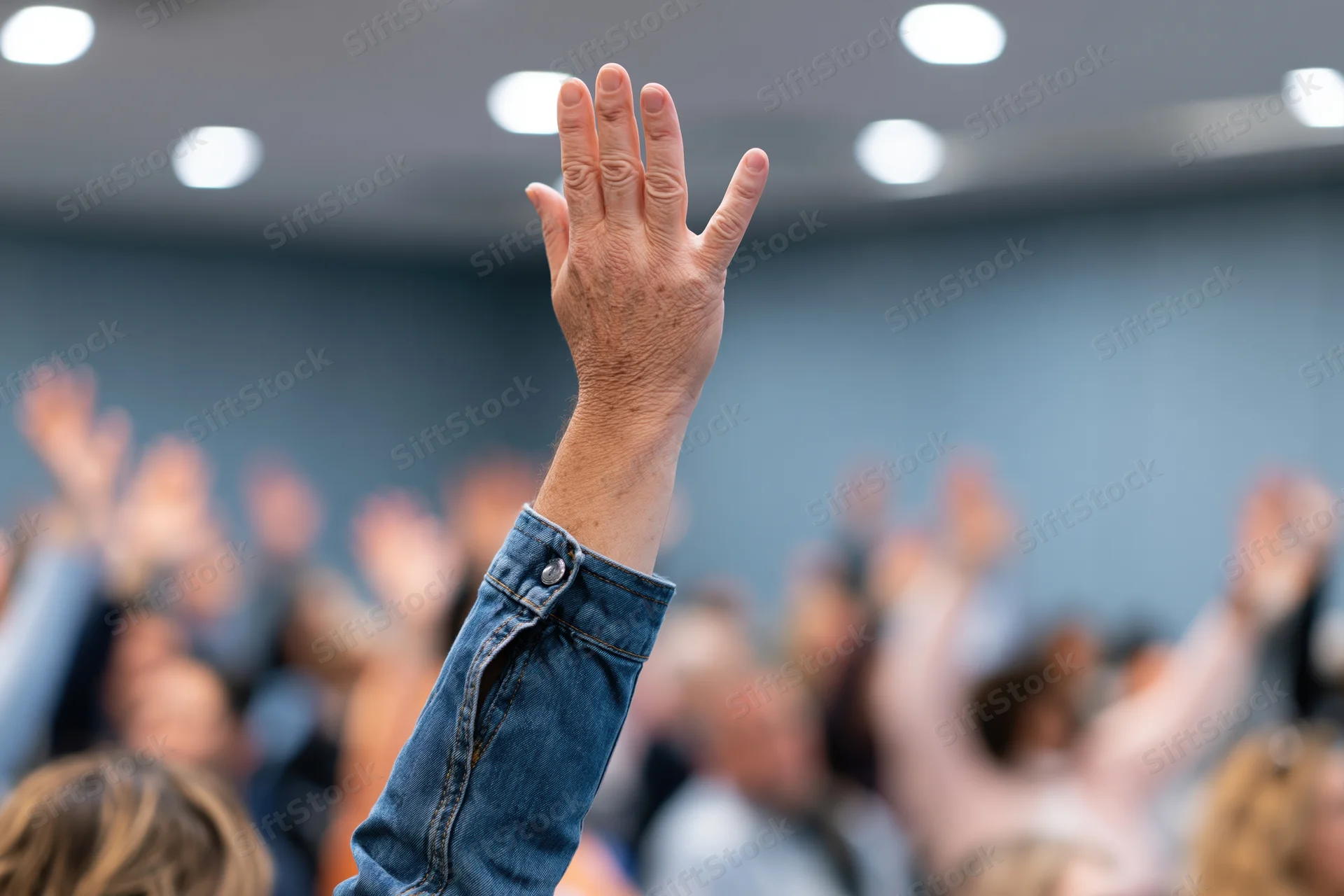 Raised hand in foreground during group event in conference room