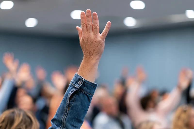 Raised hand in foreground during group event in conference room