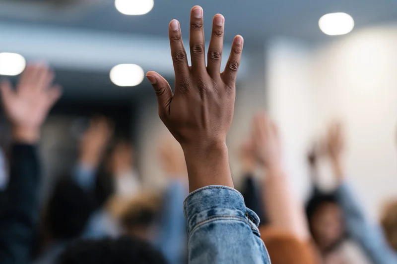 Raised hand in a classroom with blurred group of students in the background