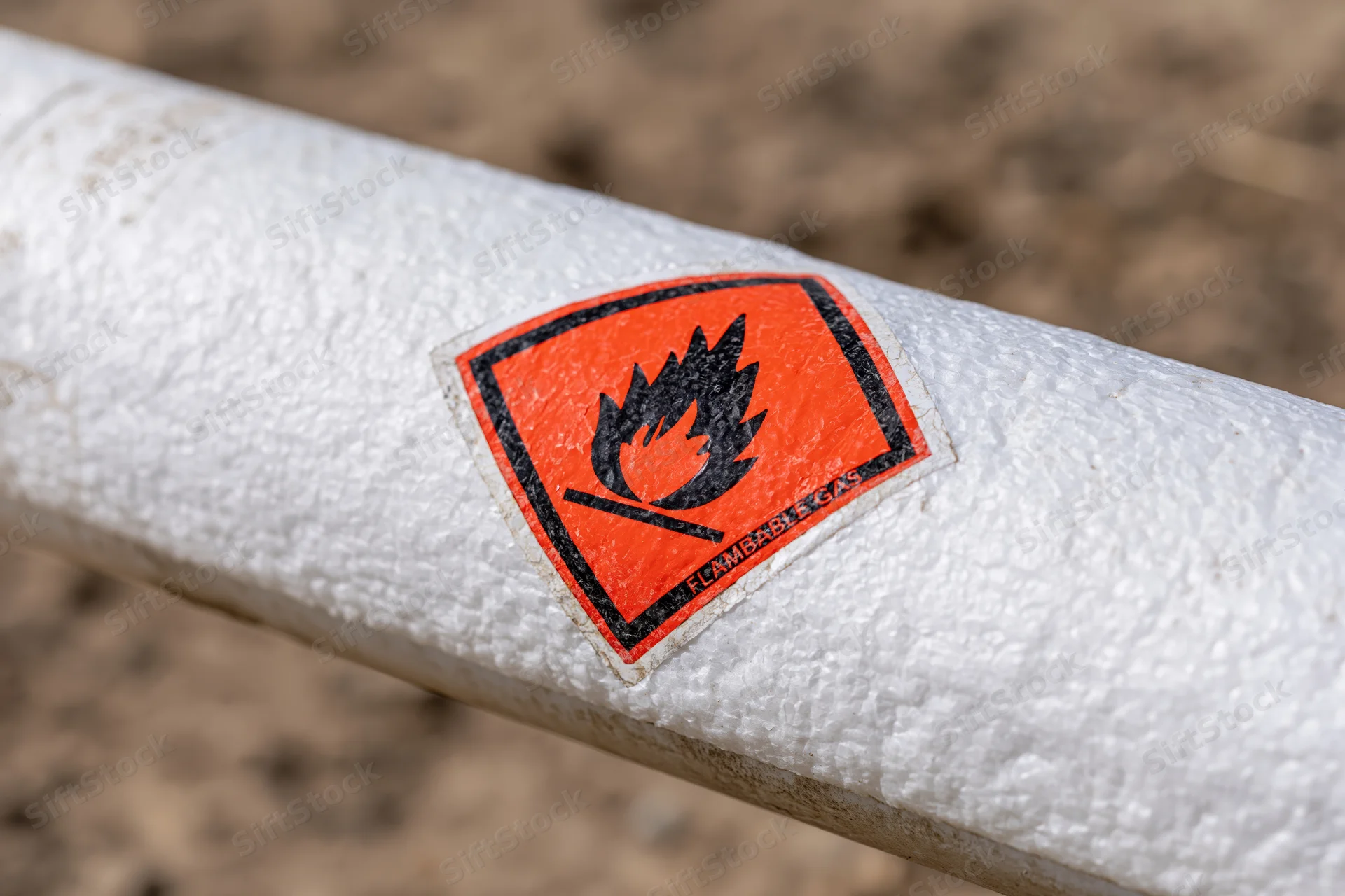 Close-up of orange diamond-shaped flammable gas hazard warning label on white textured pipeline outdoors