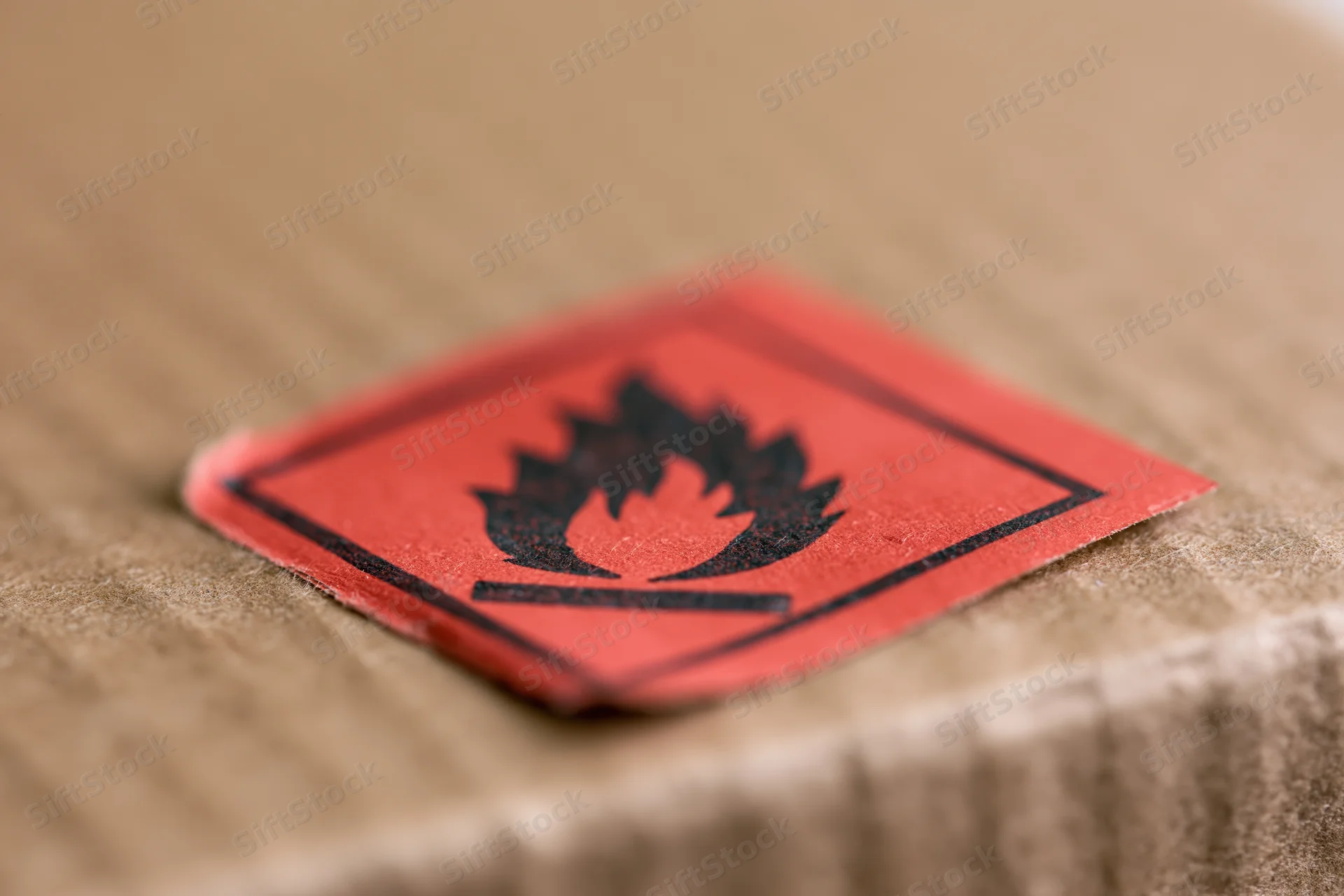Red flammable hazard warning label affixed to a cardboard box surface