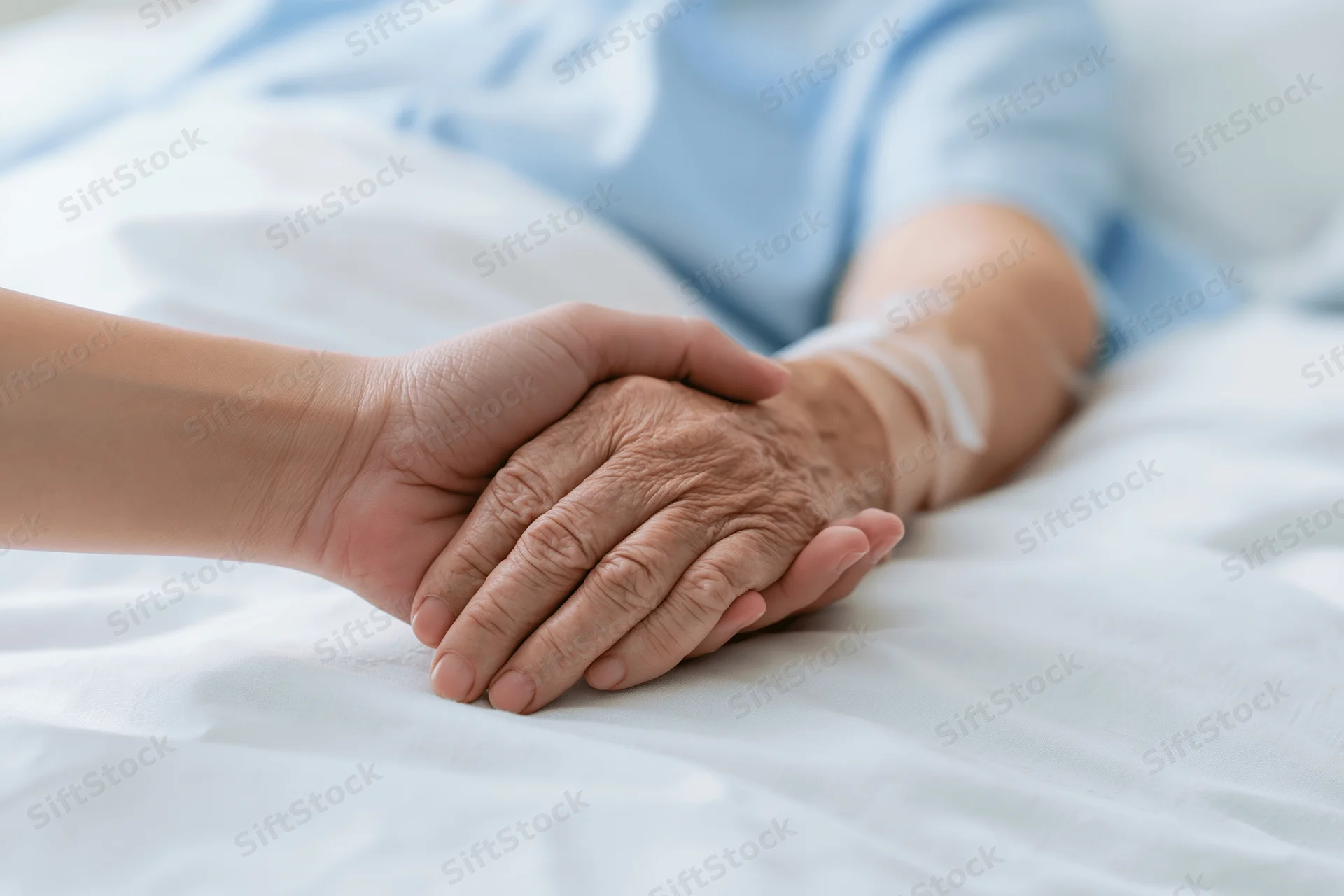 Younger person's hand gently holding elderly patient's hand on hospital bed