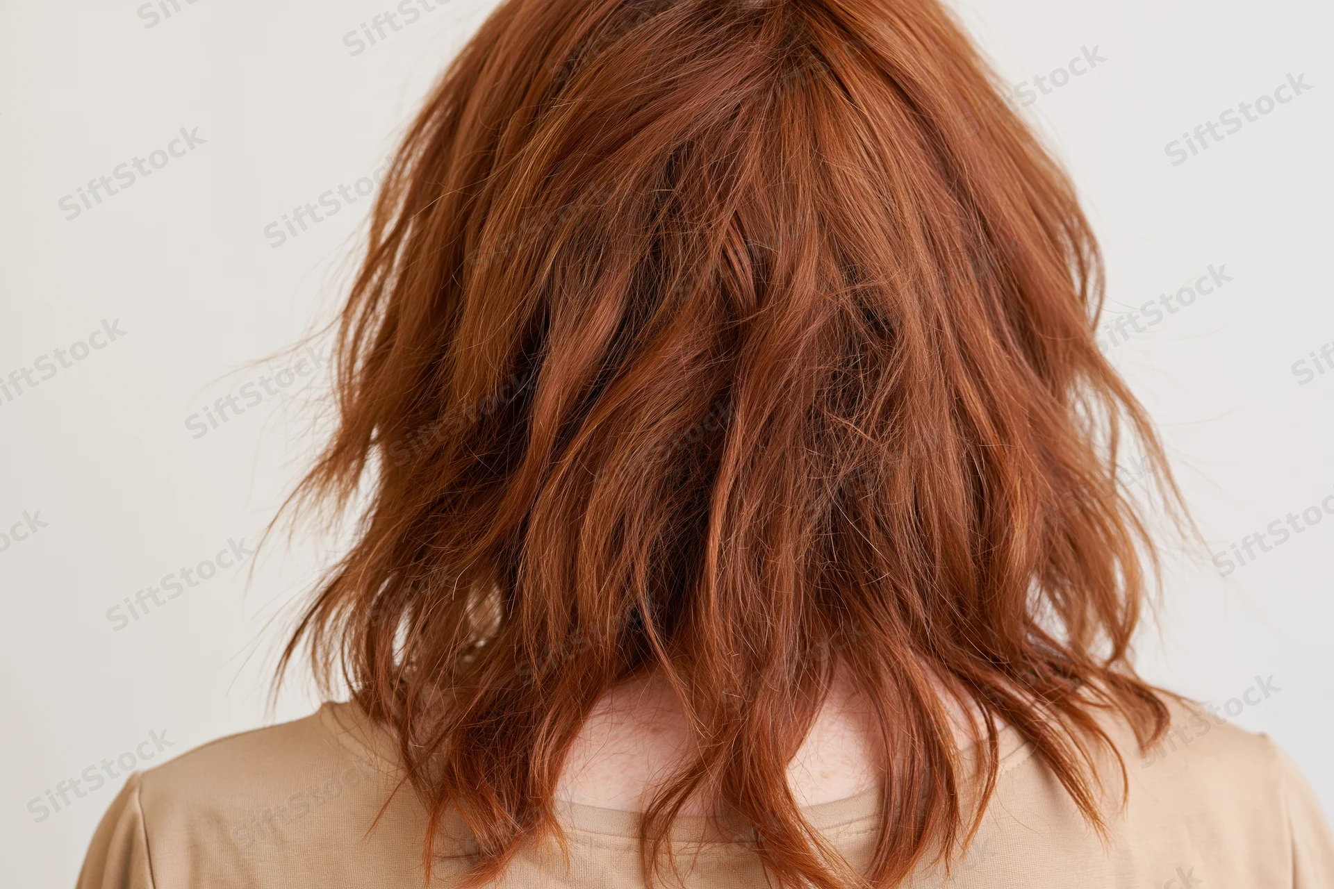 Back of a woman with dry frizzy wavy red hair, close-up view in studio setting