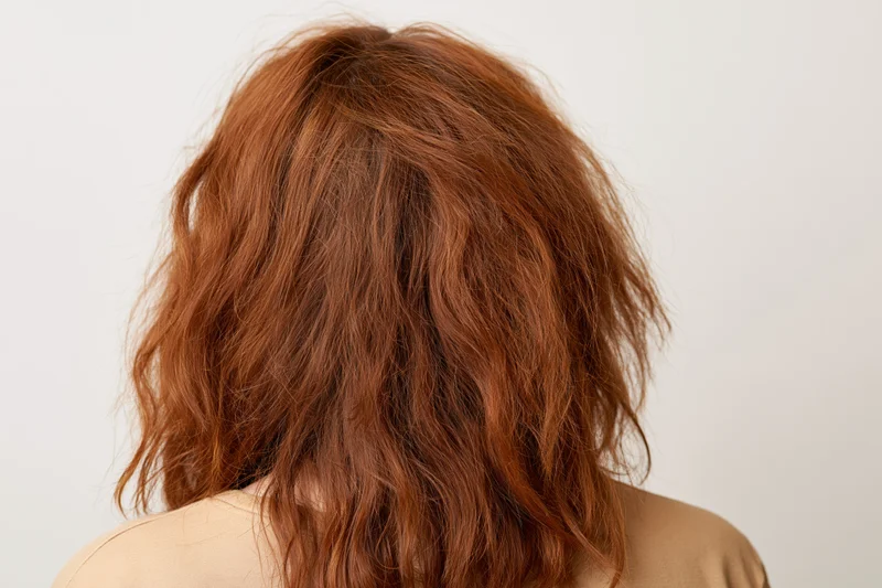 Back view of a woman with dry frizzy wavy red hair against white background