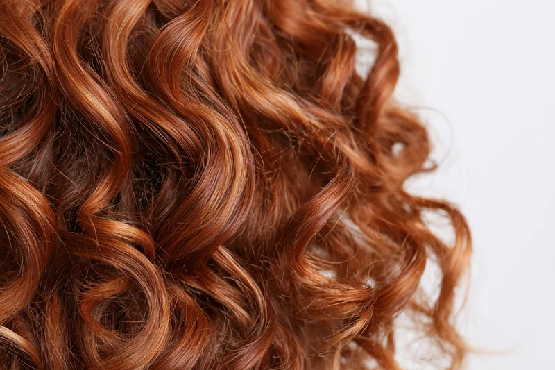Close-up of thick curly auburn red hair arranged in loose waves against white background