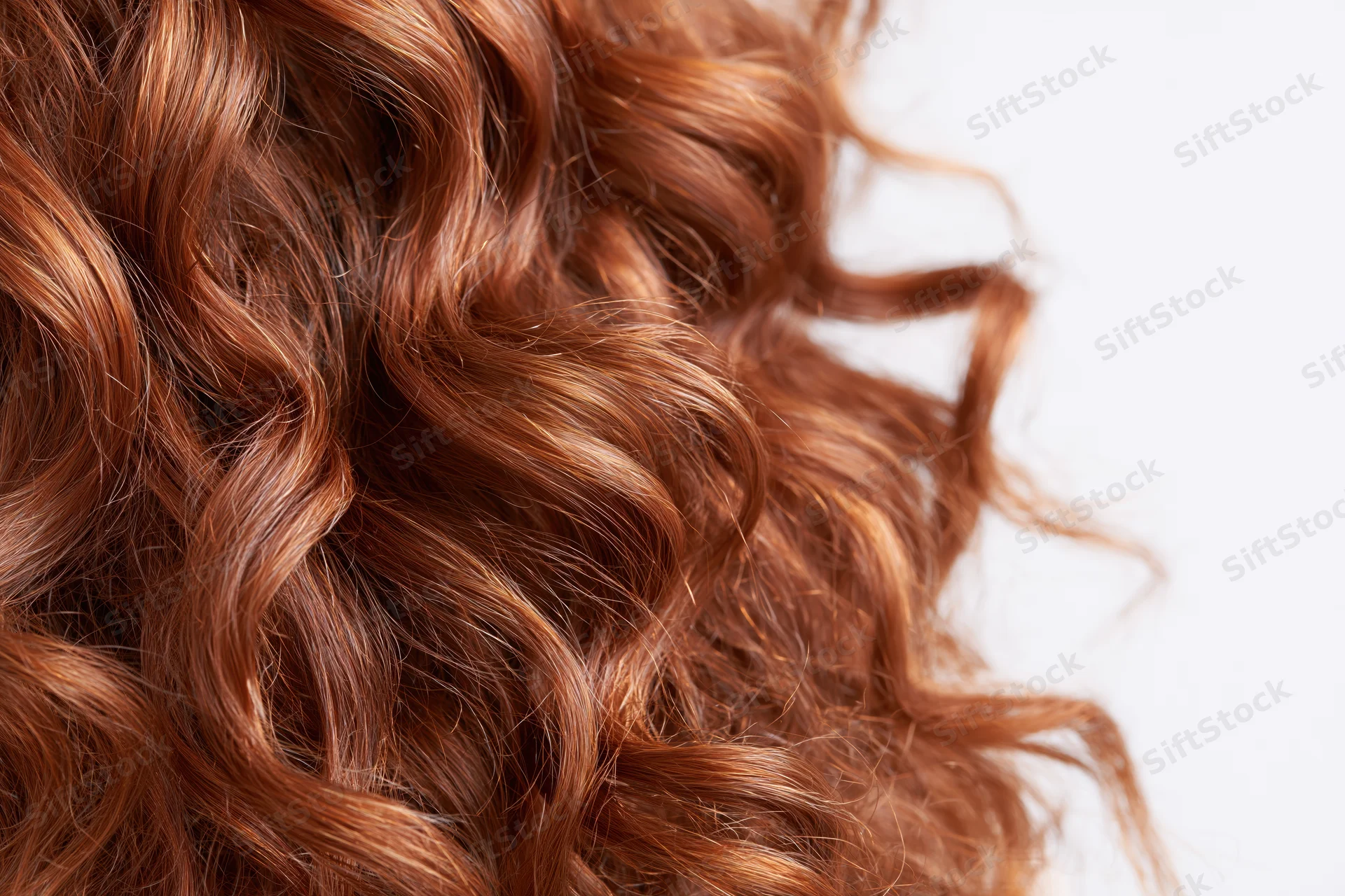 Close-up of thick curly auburn red hair arranged in loose waves against white background