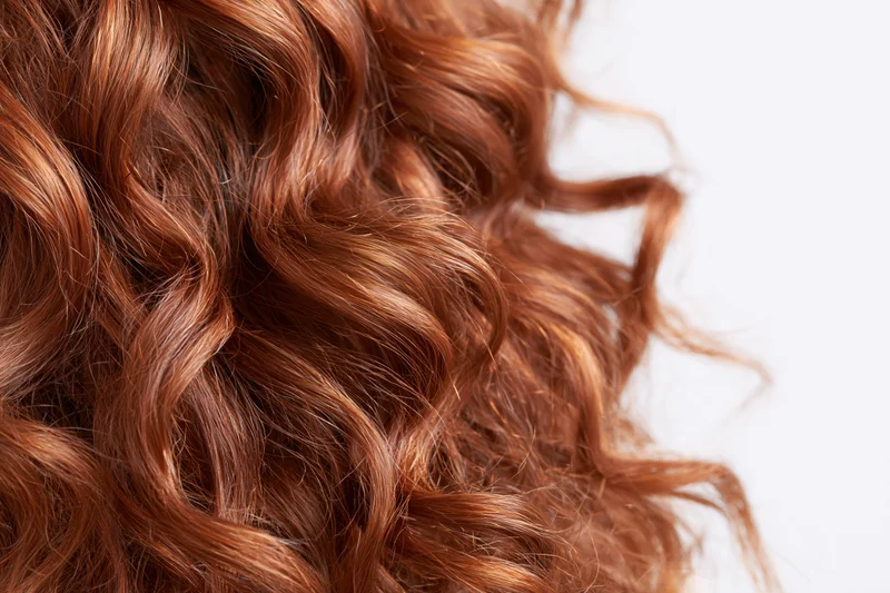 Close-up of thick curly auburn red hair arranged in loose waves against white background