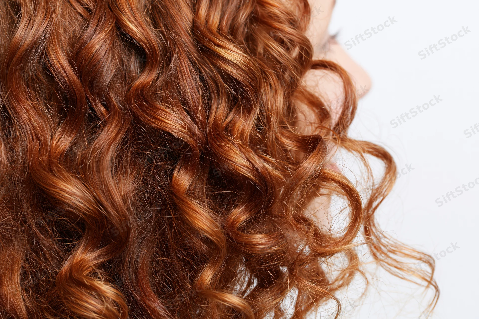 Close-up of thick curly auburn red hair arranged in loose waves on a woman's head in profile view