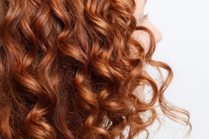 Close-up of thick curly auburn red hair arranged in loose waves on a woman's head in profile view
