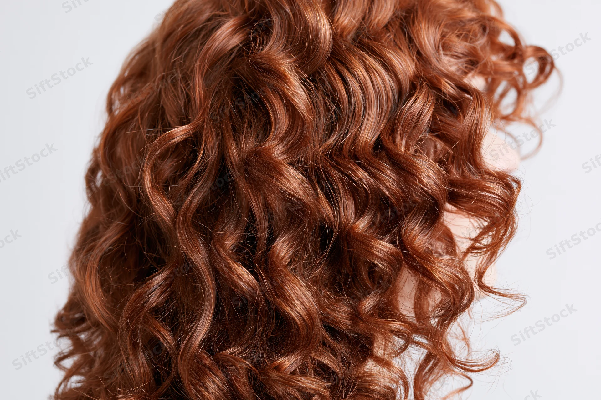 Close-up of thick curly auburn red hair arranged in loose waves against white background