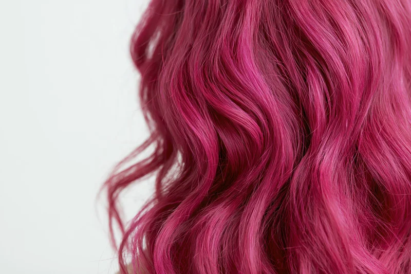 Close-up of wavy dyed magenta-pink hair with volume against white background
