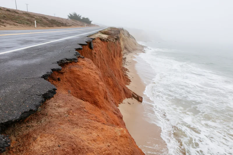 Coastal road damaged by erosion along ocean cliff with waves crashing below