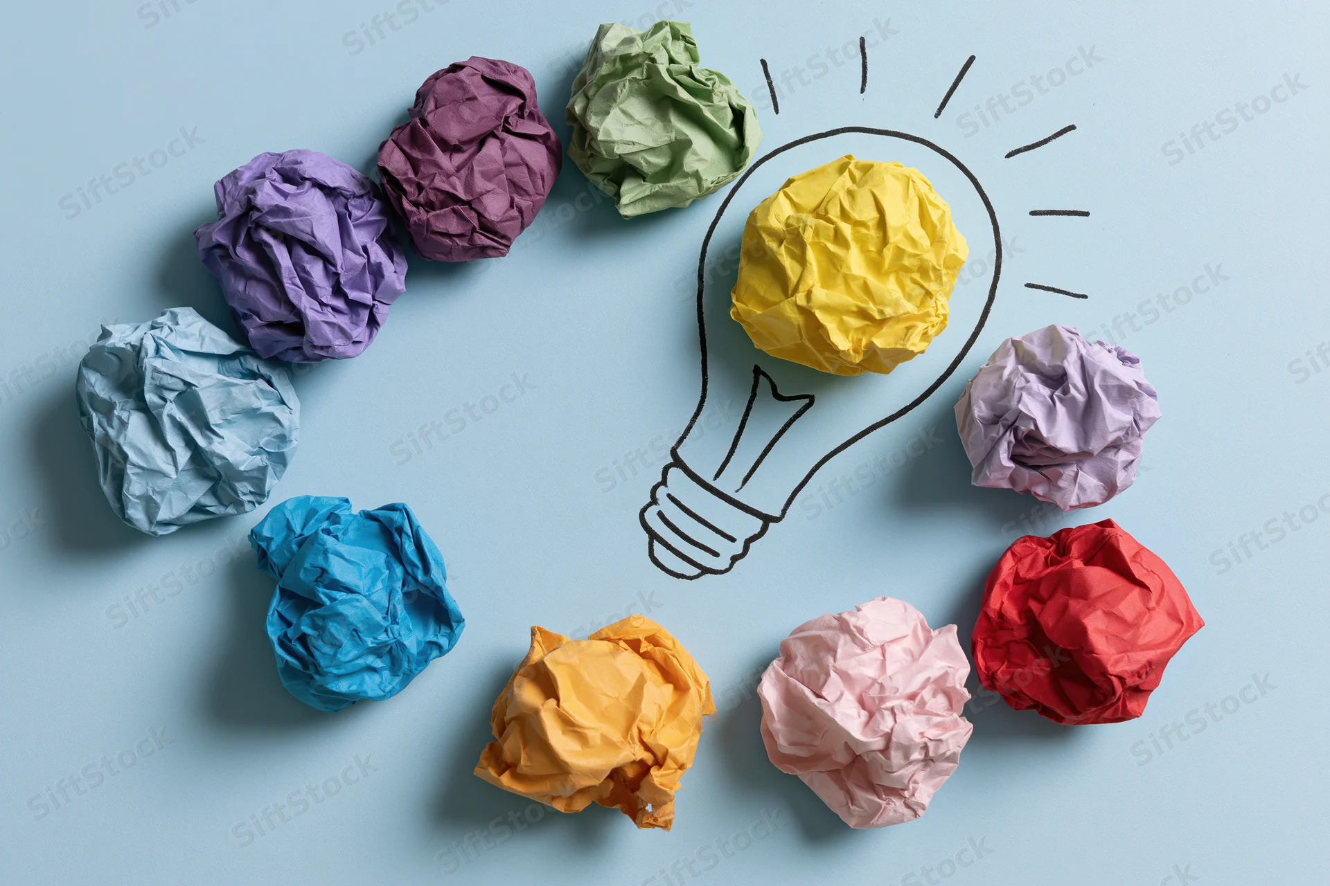 Colorful crumpled paper balls arranged around a hand-drawn lightbulb on a light blue surface
