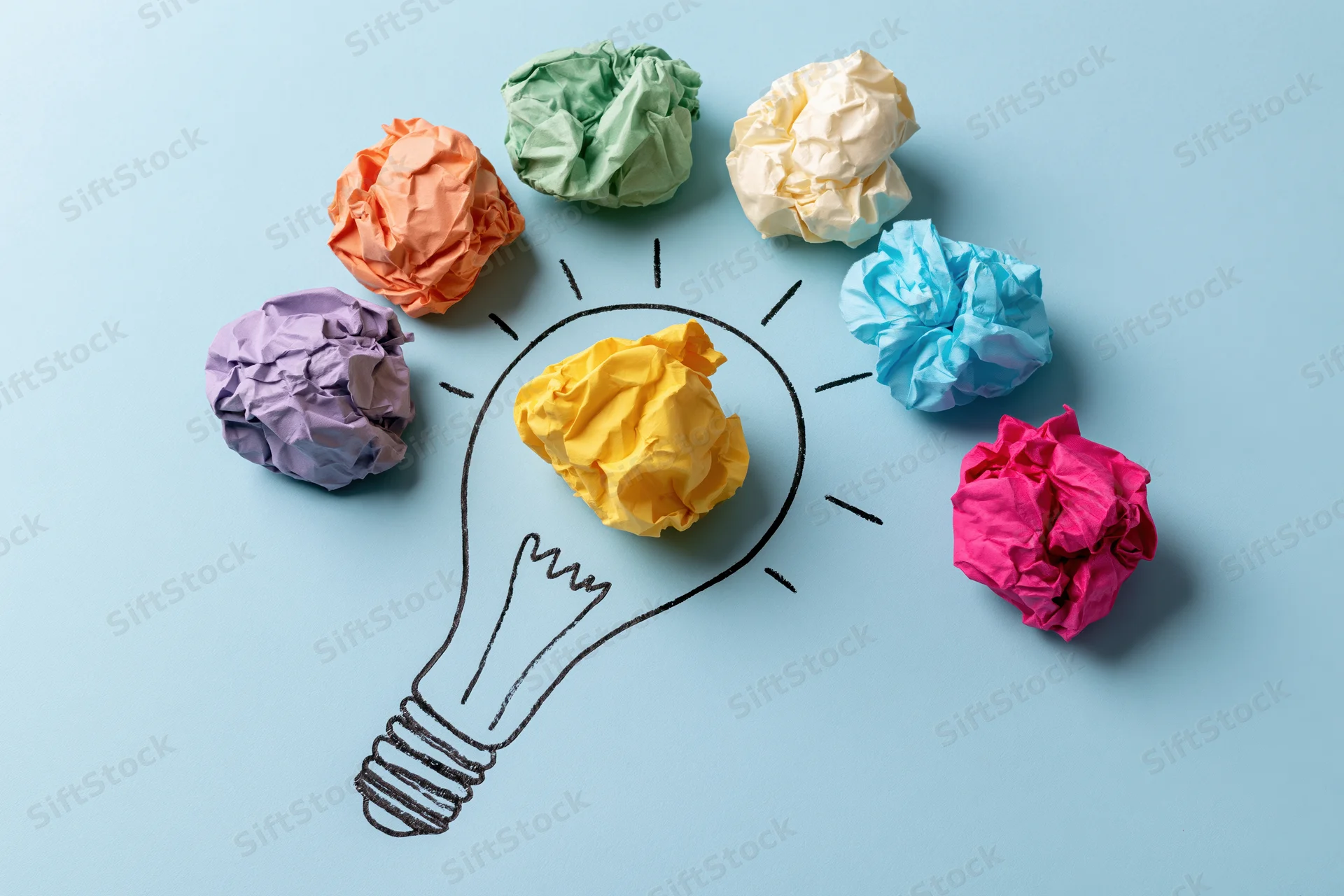 Crumpled colorful paper balls arranged around a hand-drawn lightbulb on a light blue surface