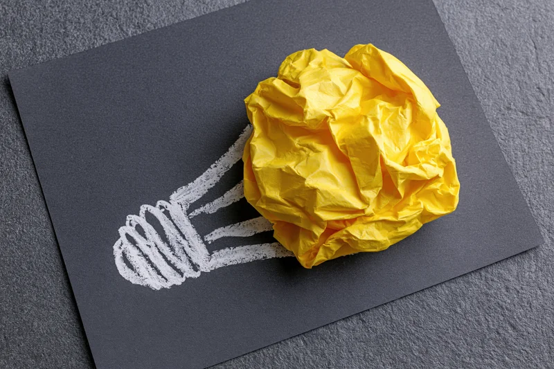 Crumpled yellow paper ball placed as bulb of hand-drawn lightbulb on dark board
