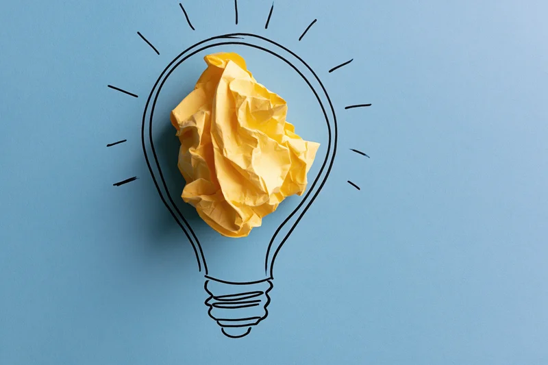 Crumpled yellow paper ball inside hand-drawn lightbulb on blue background