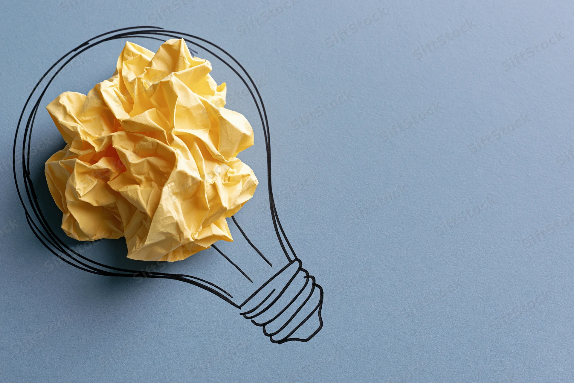 Crumpled yellow paper ball inside hand-drawn lightbulb outline on blue surface