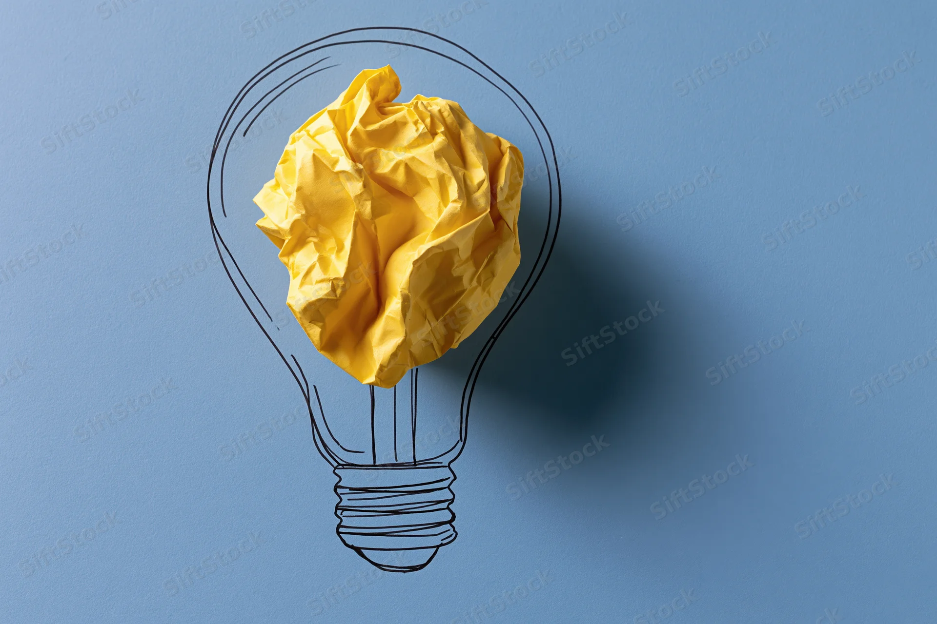 Crumpled yellow paper ball inside hand-drawn lightbulb outline on blue background