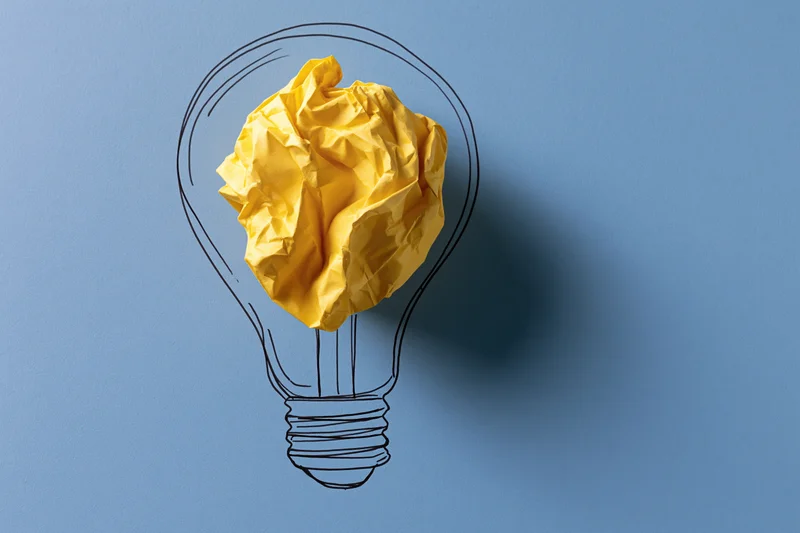 Crumpled yellow paper ball inside hand-drawn lightbulb outline on blue background