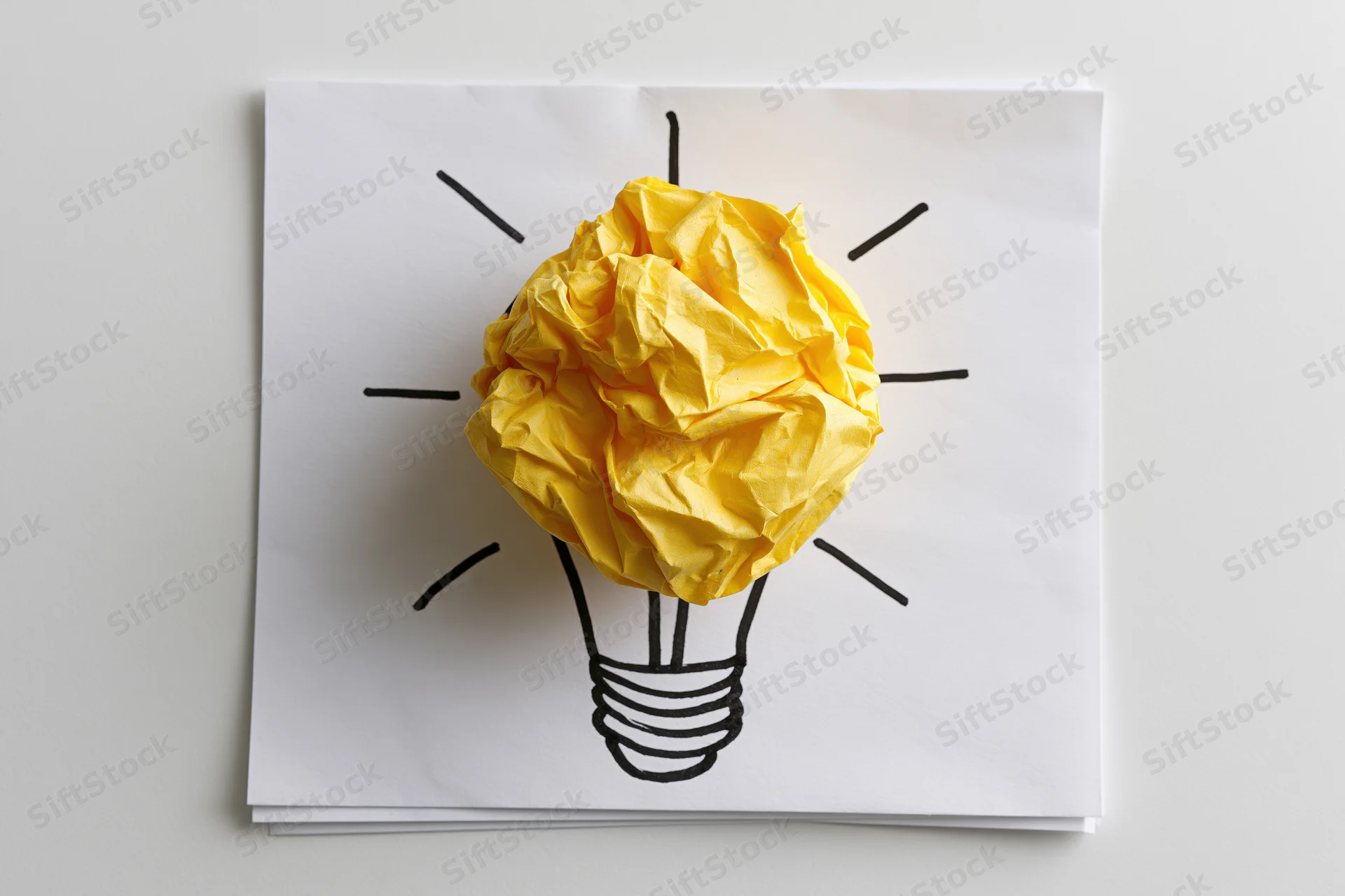 Crumpled yellow paper ball forming a lightbulb on a hand-drawn sketch on white paper