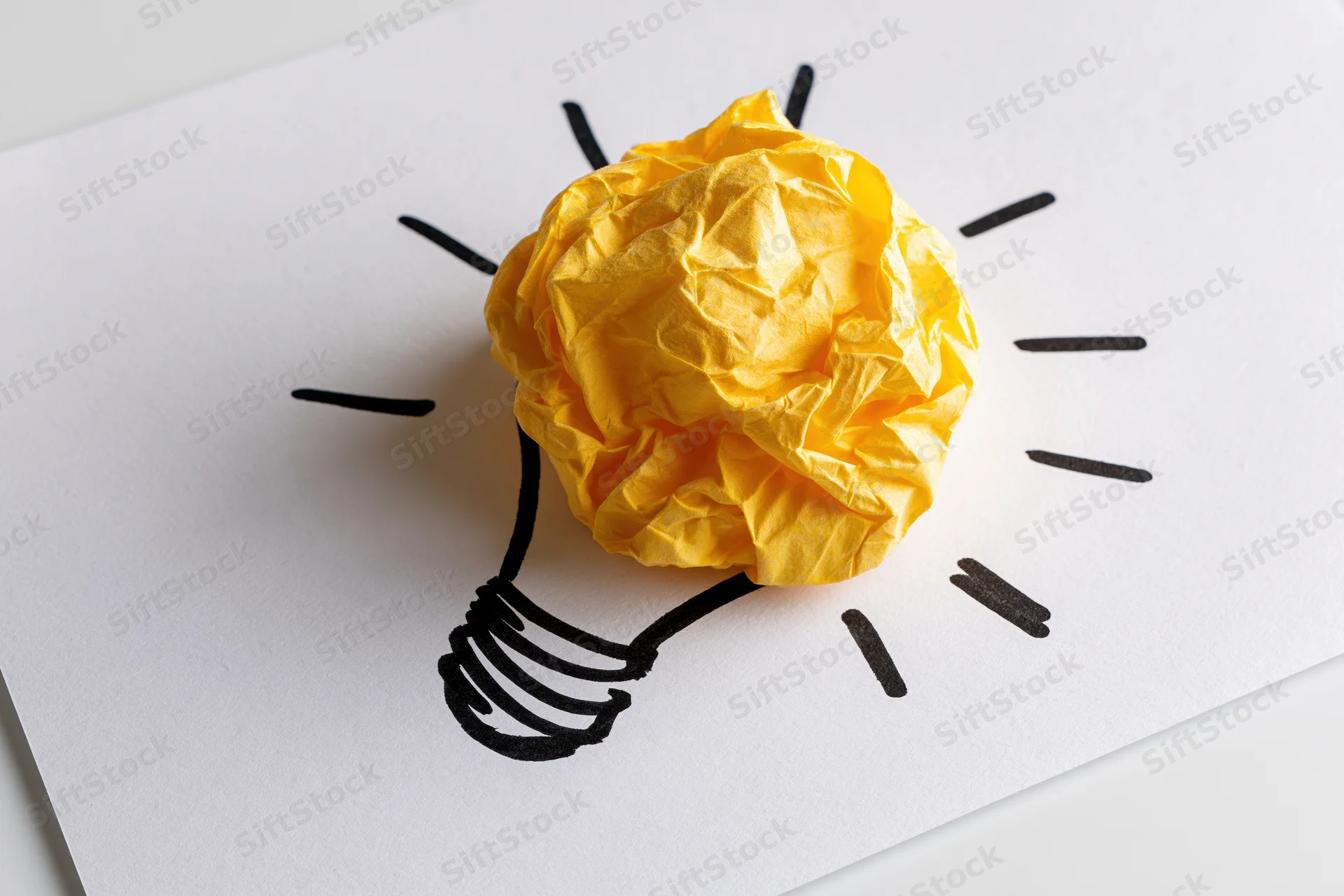 Crumpled yellow paper ball forming a lightbulb on a hand-drawn sketch on white paper