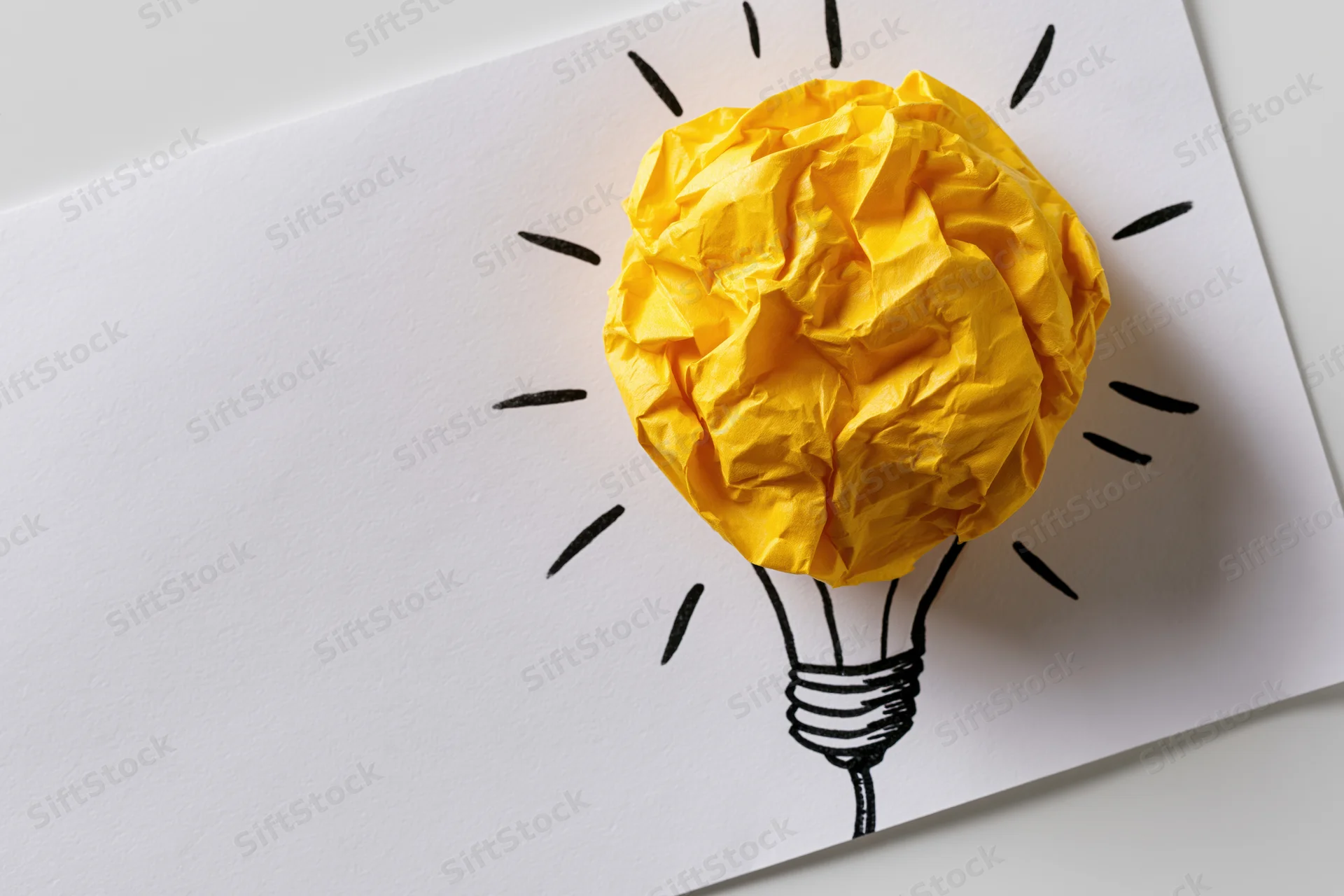 Crumpled yellow paper ball as lightbulb bulb on hand-drawn sketch on white paper