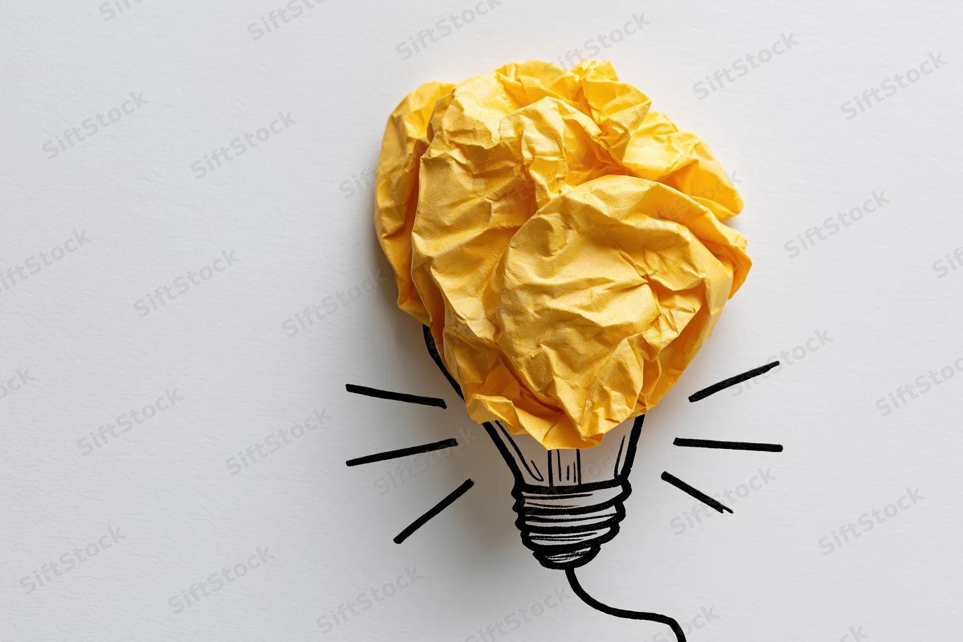Crumpled yellow paper ball shaped like a lightbulb with hand-drawn base and rays on white surface