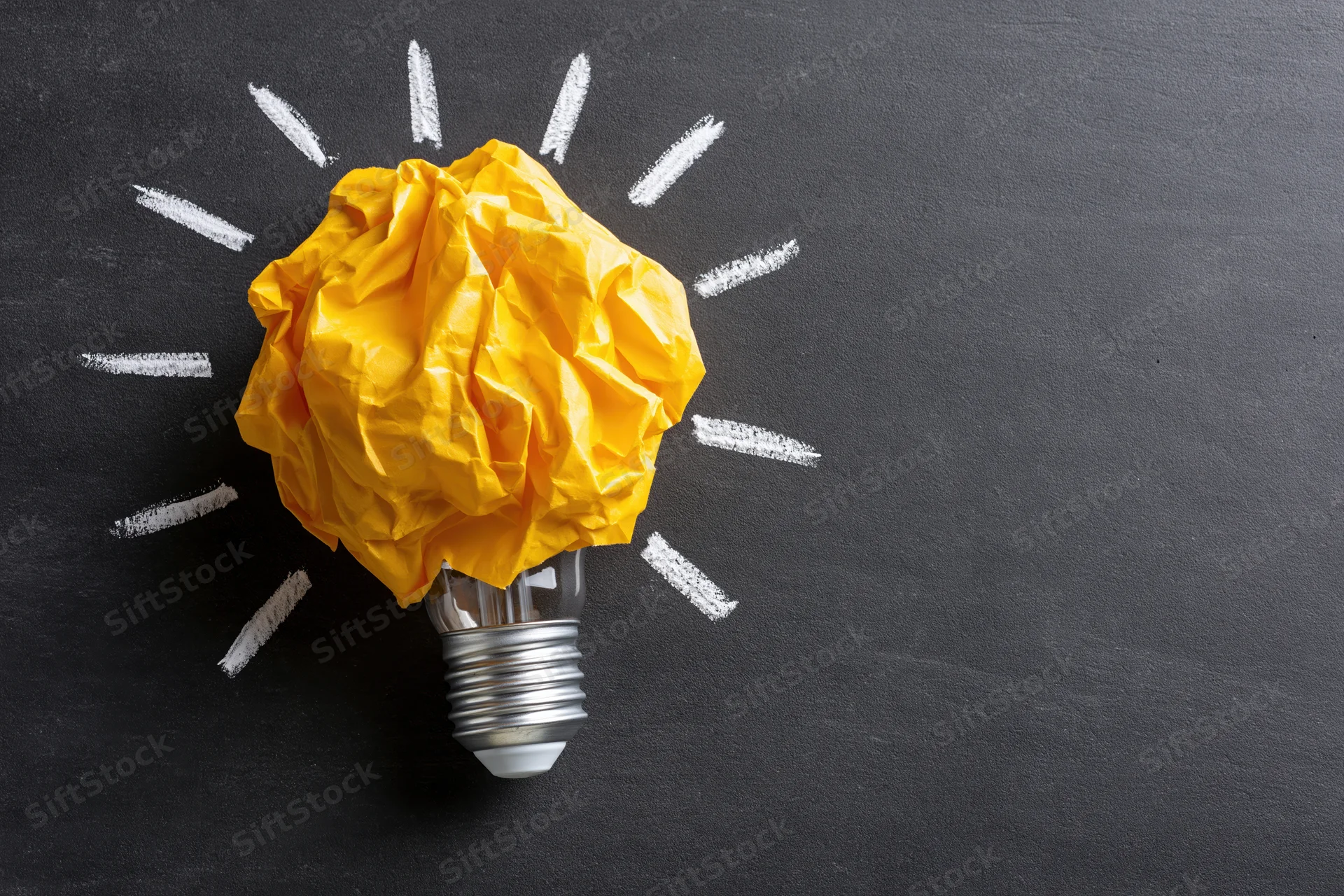 Crumpled yellow paper ball on a lightbulb with chalk-drawn rays on a blackboard