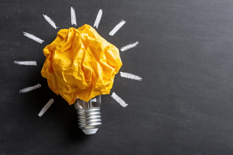 Crumpled yellow paper ball on a lightbulb with chalk-drawn rays on a blackboard