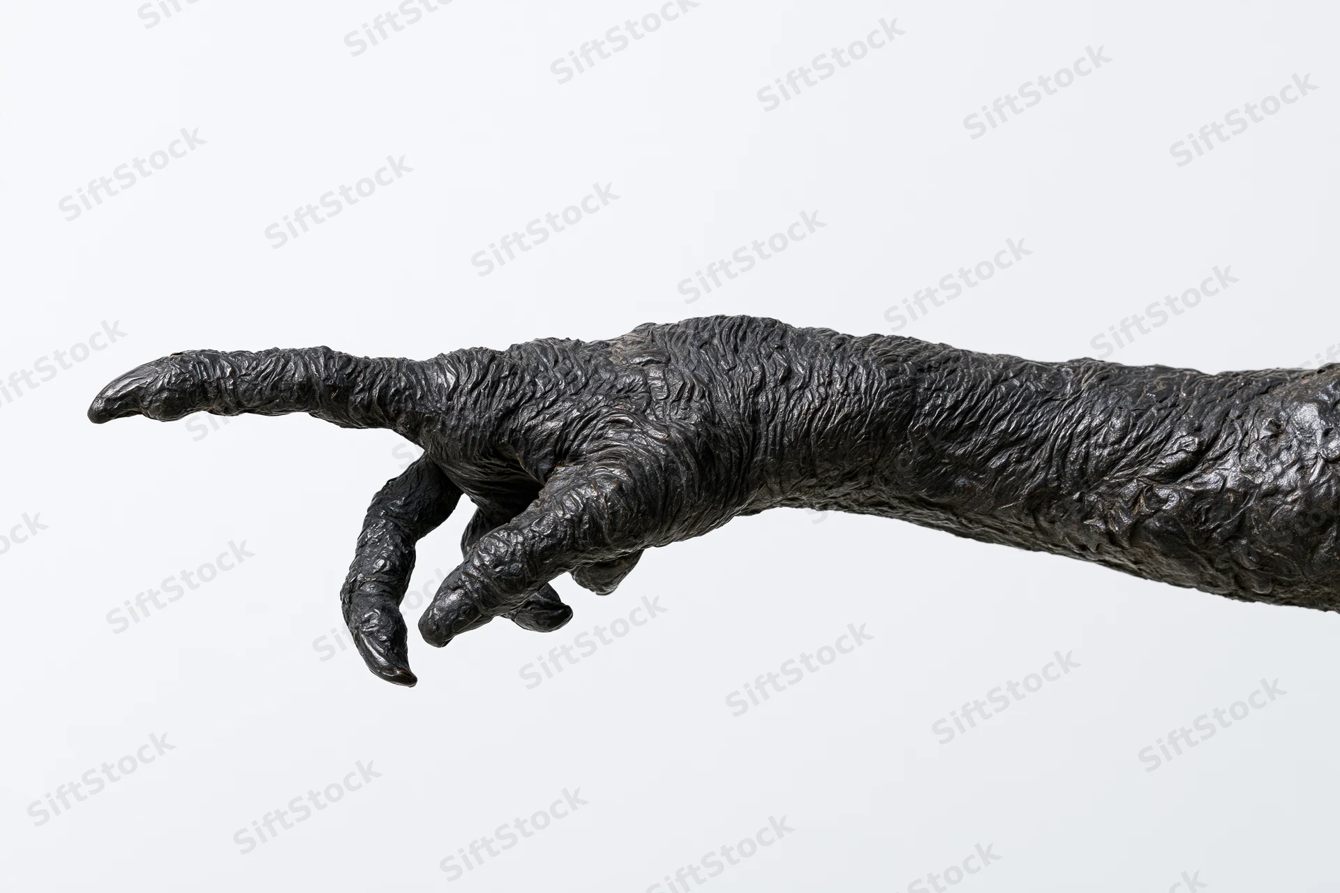 Dark bronze sculpture of a clawed creature hand pointing forward against white background