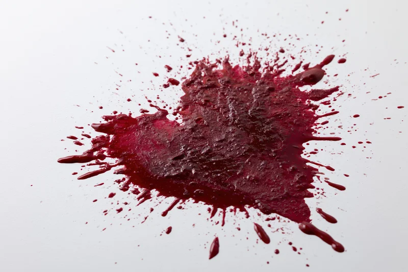 Crimson paint splatter forming a rough heart shape on white surface
