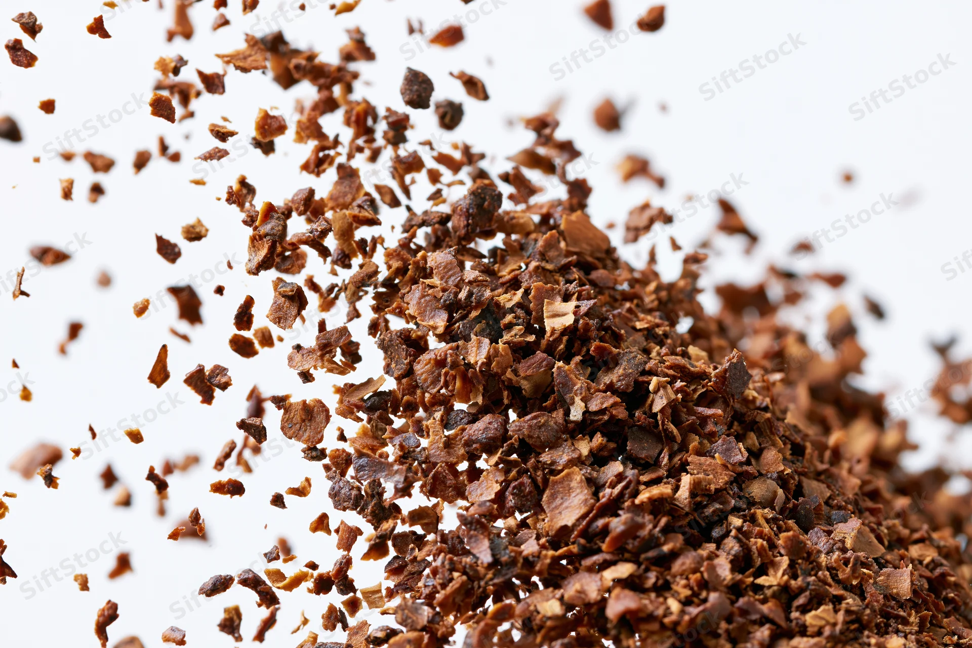 Pile of dried brown herb flakes scattered and falling against white background