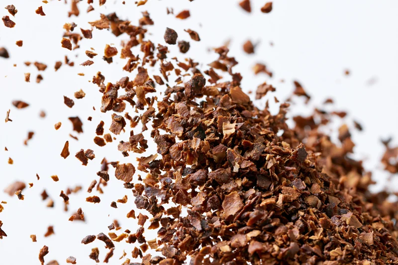Pile of dried brown herb flakes scattered and falling against white background