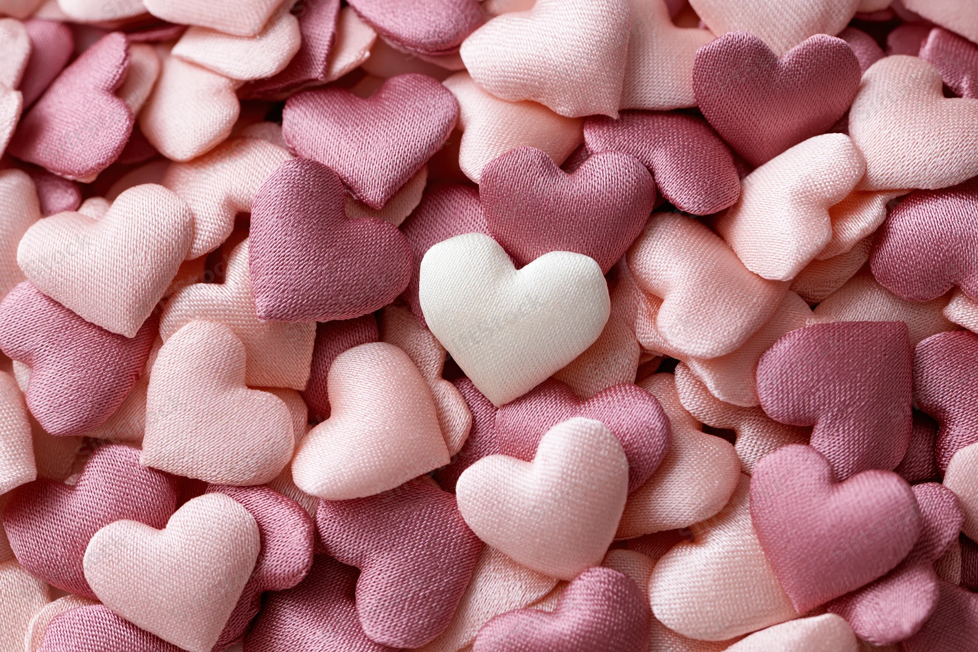 Pile of small fabric hearts in pink and white tones filling the frame