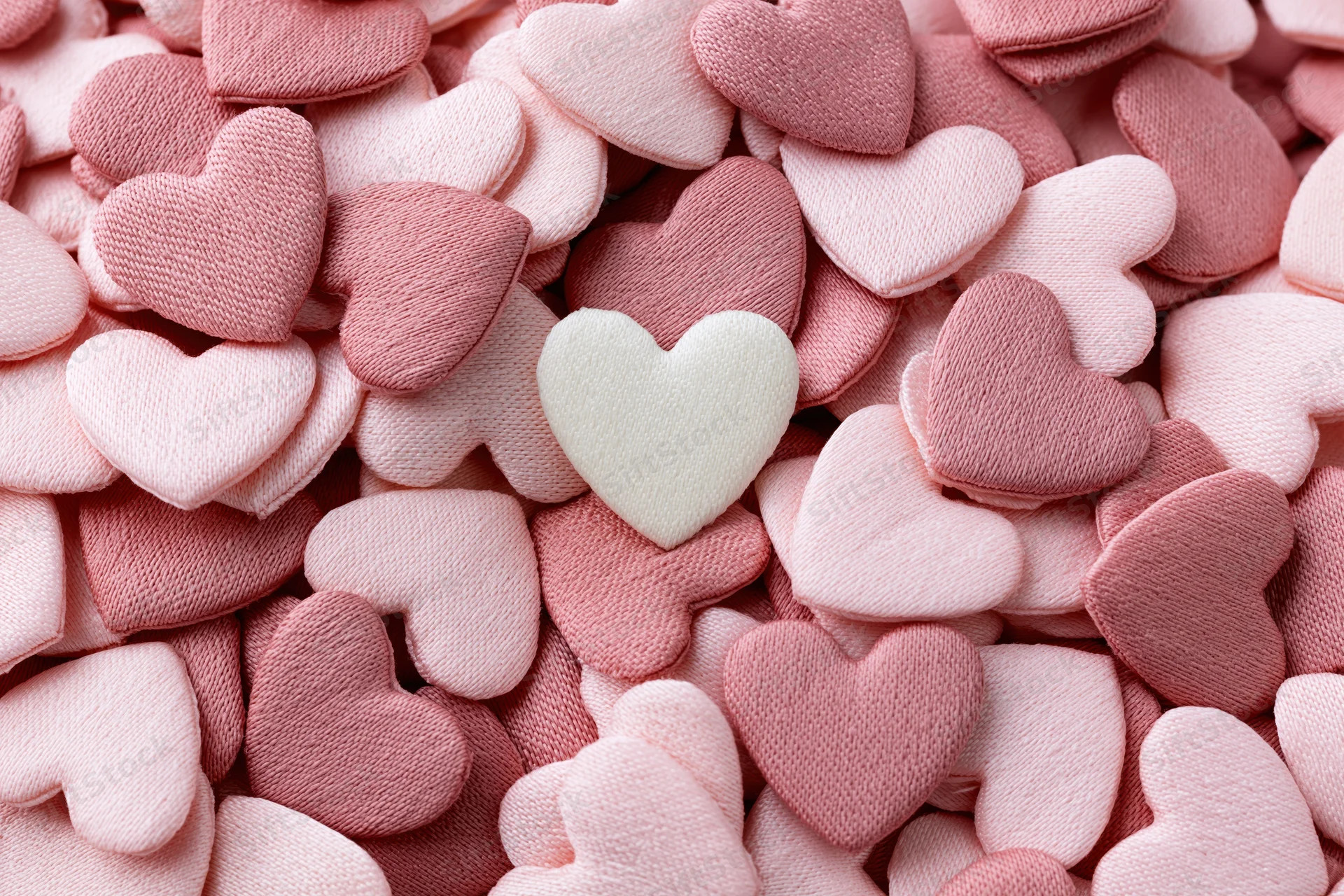 Pile of small fabric hearts in pink and white tones filling the frame