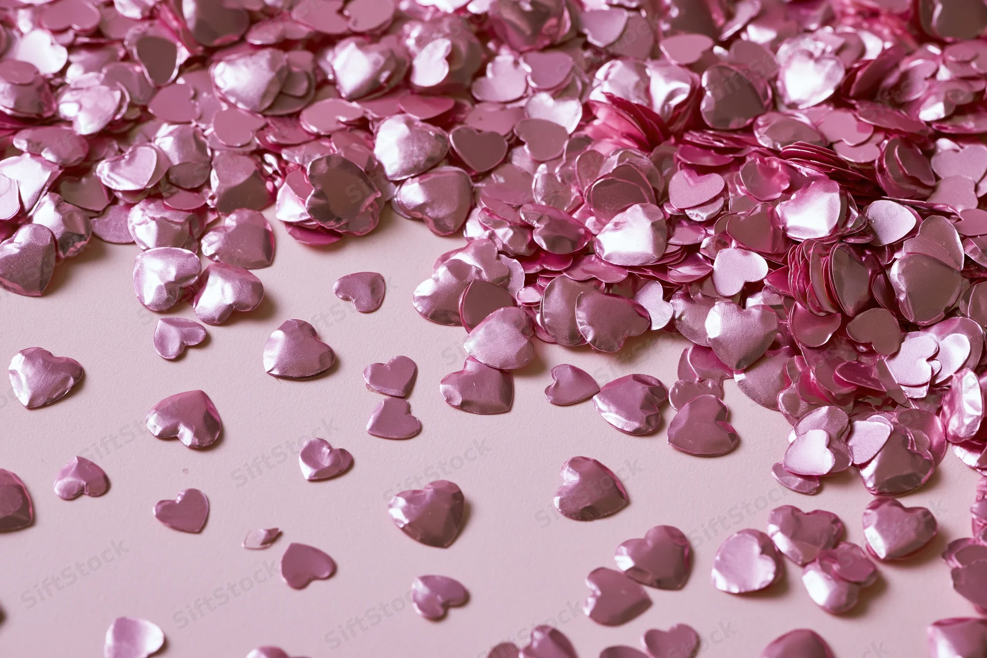 Shiny pink heart-shaped foil confetti scattered across a soft pink surface