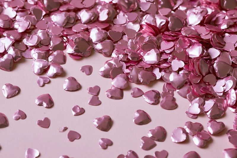 Shiny pink heart-shaped foil confetti scattered across a soft pink surface