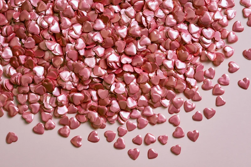 Scattered shiny pink foil heart-shaped confetti on a light pink surface