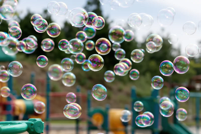 Soap bubbles floating in midair above a children's playground with colorful equipment in the background