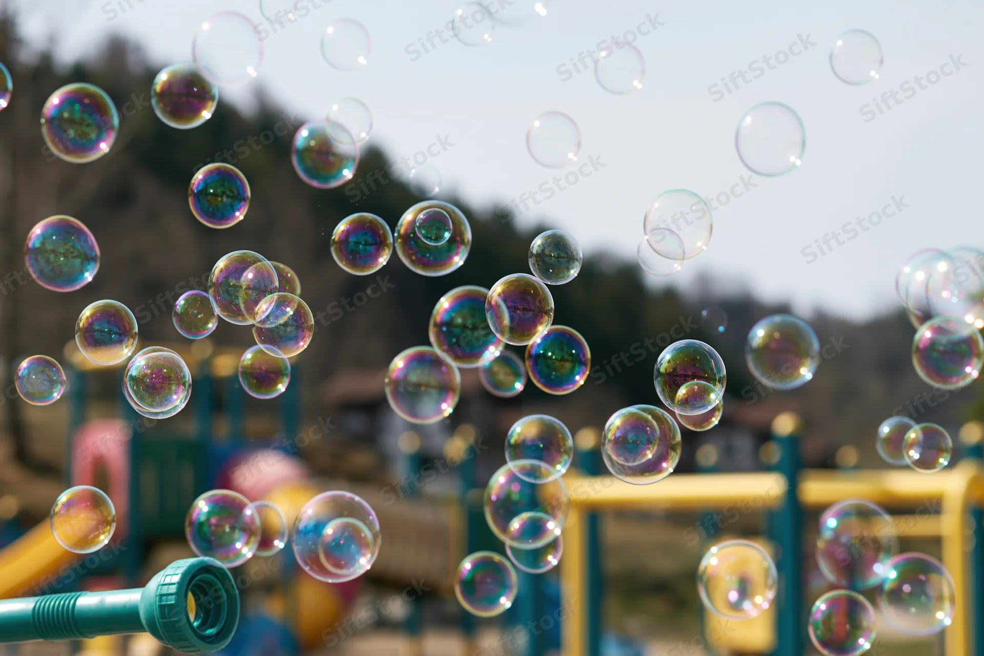 Soap bubbles floating in midair above a children's playground with a bubble blower in the foreground