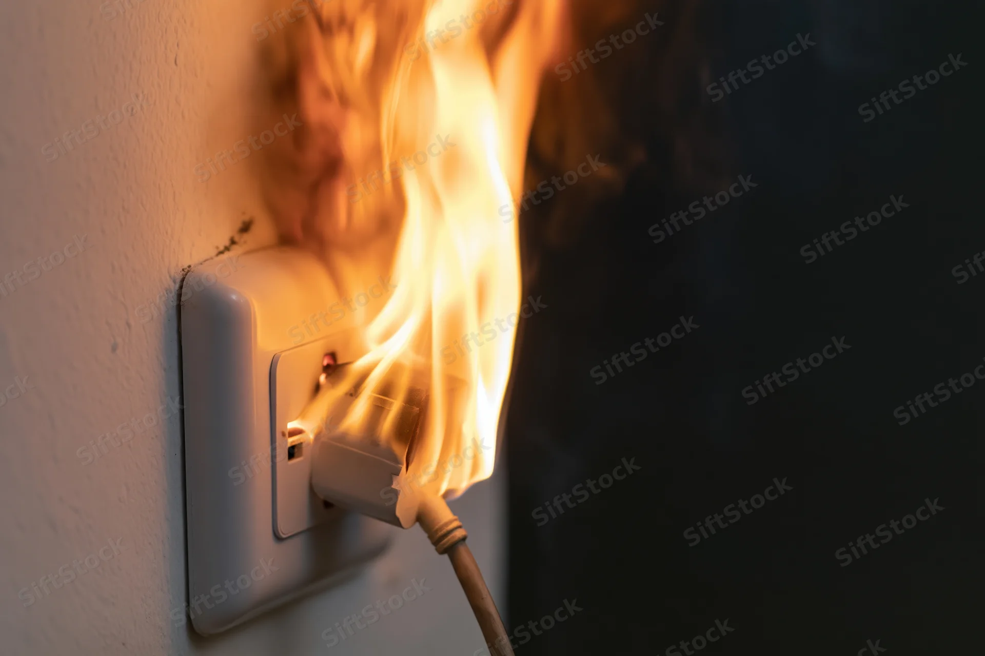Flames erupting from a white electrical wall outlet with a plugged-in cord