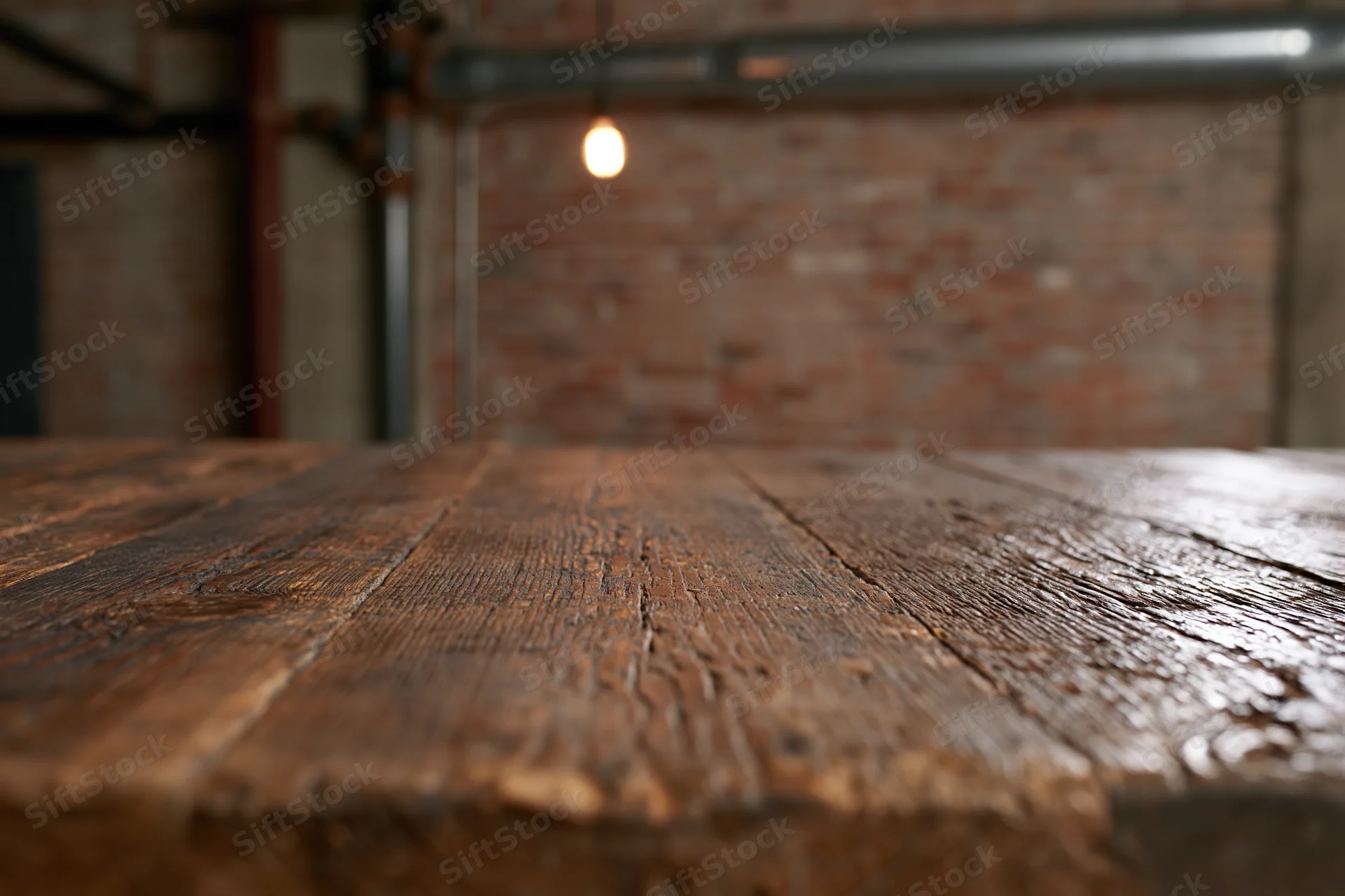 Dark weathered wooden table surface in industrial loft interior with brick wall and pendant light in background
