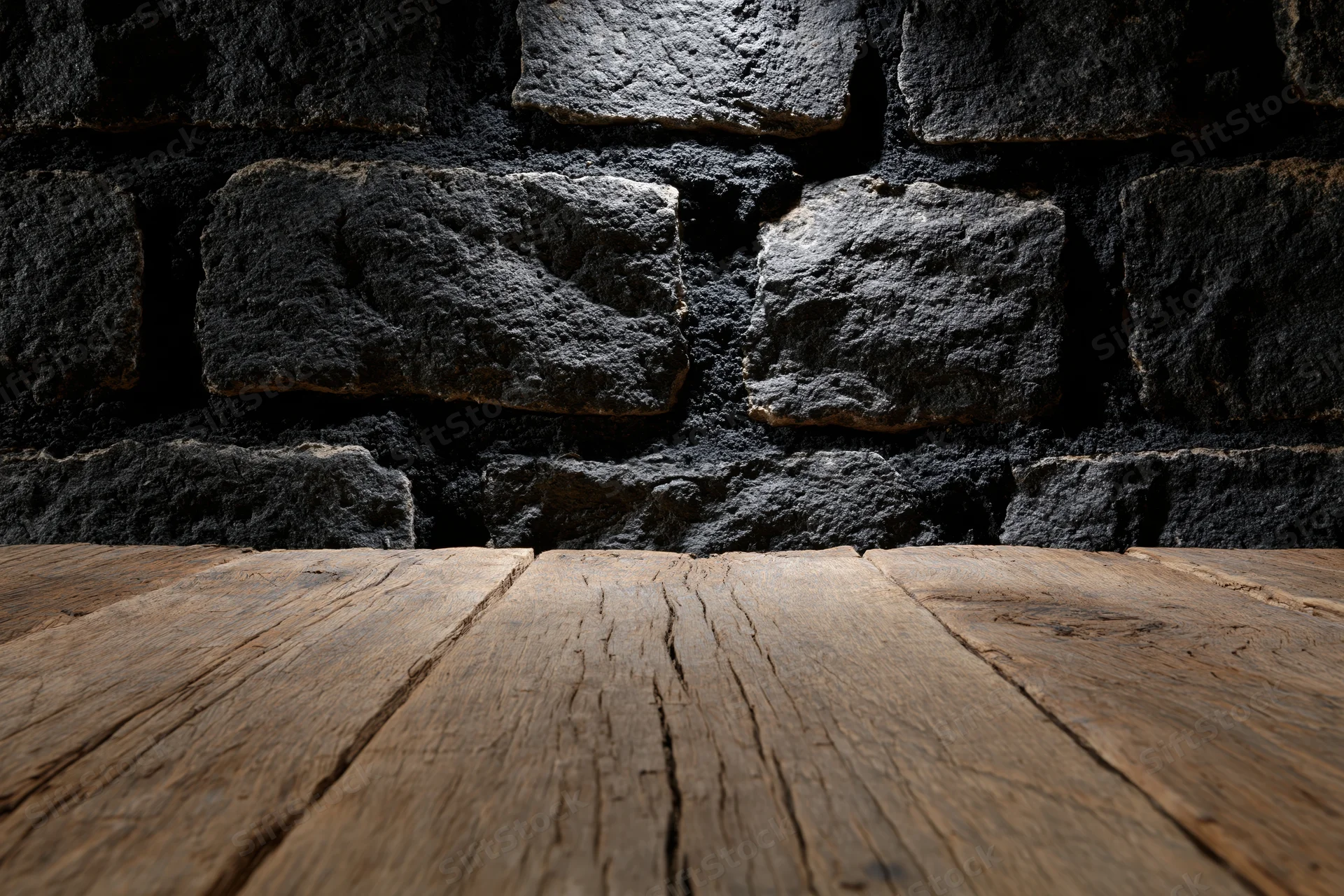 Weathered wooden table surface in front of dark stone wall with copyspace
