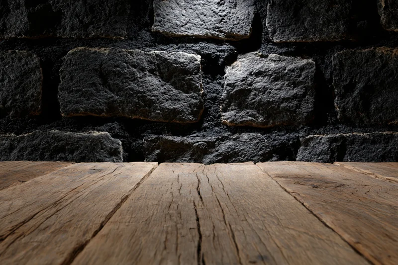 Weathered wooden table surface in front of dark stone wall with copyspace