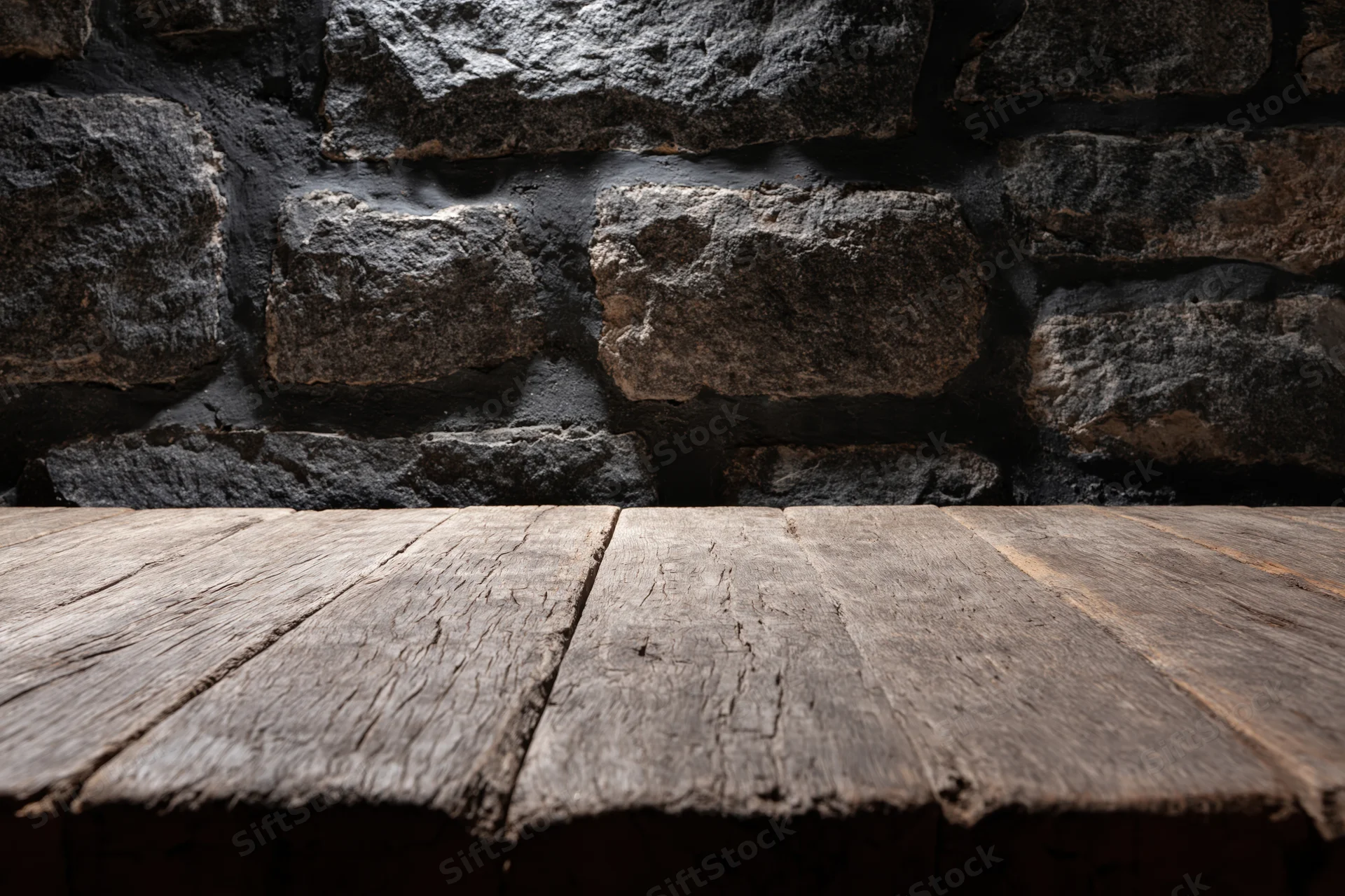 Weathered wooden table surface in front of dark stone wall with copyspace