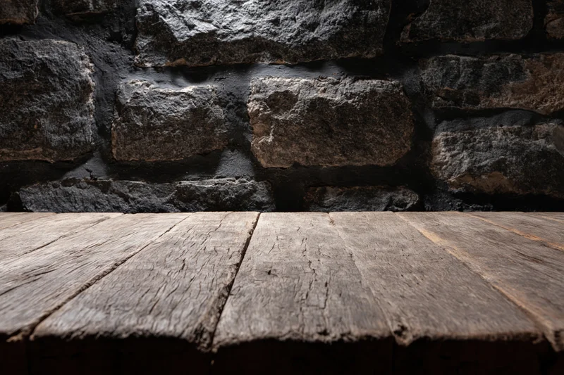 Weathered wooden table surface in front of dark stone wall with copyspace