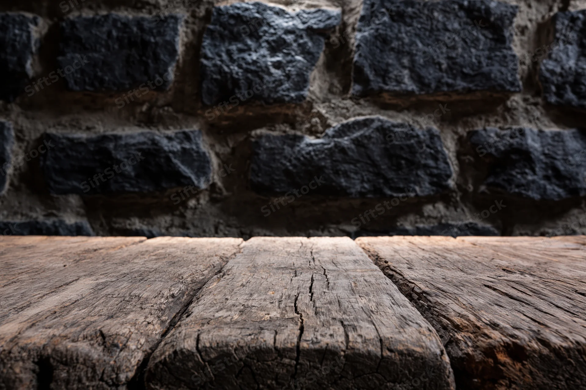 Weathered wooden table surface in front of dark stone brick wall