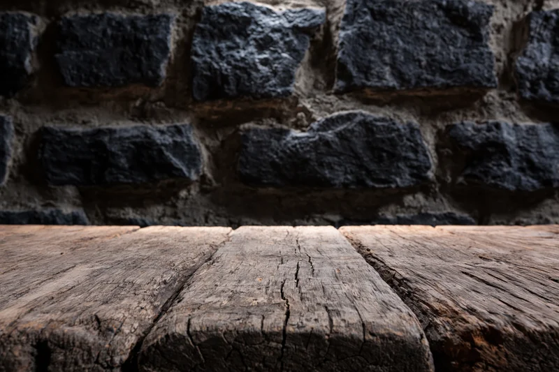 Weathered wooden table surface in front of dark stone brick wall
