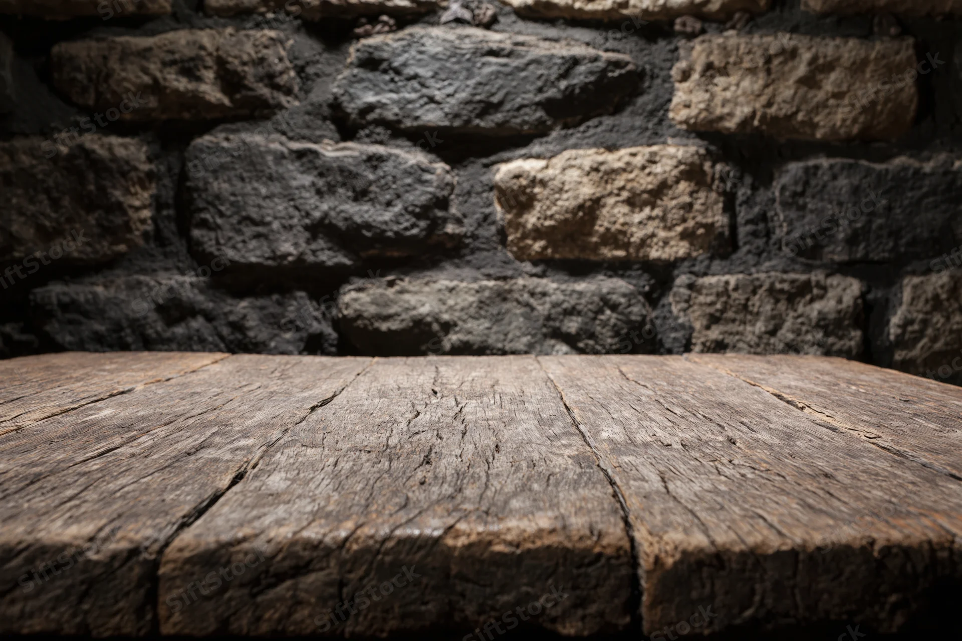 Weathered wooden table surface in front of dark stone wall with copyspace